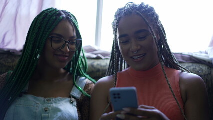 Wall Mural - Female friend sharing cellphone screen. Two young black women looking at smartphone device