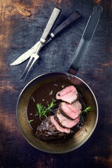 Wall Mural - Traditional German venison roast with juniper berry and rosemary in spicy red wine sauce served as top view in a frying pan
