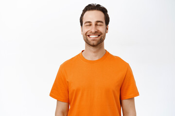 Smiling happy man with closed eyes, dreaming of smth, thinking with pleased carefree face, standing over white background