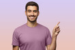 © Damir Khabirov - Attractive young man in t-shirt pointing right with finger, isolated on purple background