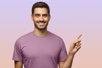 Wall Mural - Handsome smiling male in t-shirt pointing right with finger isolated on purple