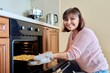 © Valerii Honcharuk - Middle-aged woman with cooked meat taking baking sheet out of oven