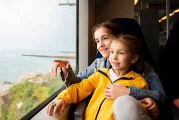 Two sister girls look out the window of a train at the sea.The girls are talking and having fun. Journey. Reflection. Vacation. Summer. Family vacation.