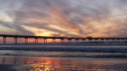 Wall Mural - Silhouette of people walking, pier on piles in sea water. Ocean waves and dramatic sky at sunset. California coast, beach or shore vibes at sundown. Summertime seascape. Seamless looped cinemagraph.