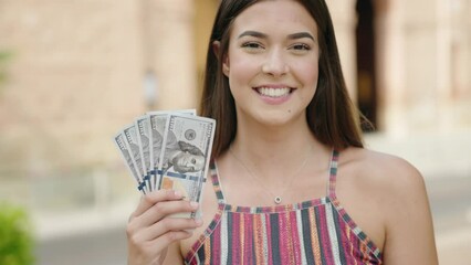 Wall Mural - Young beautiful hispanic woman smiling confident holding dollars at street