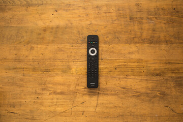 Television remote control on rustic wooden desk.