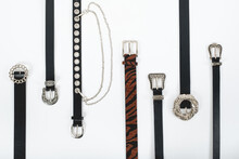 Different Types Of Black Leather And Animal Print Belts With Variety Of Buckles On White Background