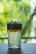 © Dontree - Americano coffee mixed with cool water in a clear glass can be seen in layers. Behind it is a refreshing green bokeh.