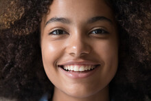 Front Face View Beautiful Smiling Teen 17s Girl Staring At Camera. Close Up Portrait Happy American Curly-haired Adolescent Having Straight Perfect White Teeth, Ideal Skin, Cute Appearance Look At Cam