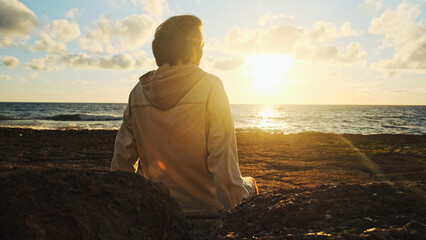 Wall Mural - Man on a beach is looking distance during beautiful summer sunset. Human looks to the sun over horizon in the morning while sunrise. Happy person contemplates the beauty of nature. Freedom concept.