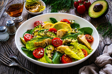 Wall Mural - Fresh vegetable salad - avocado, artichoke, lettuce, cherry tomatoes, cucumber, arugula and spinach on wooden table 