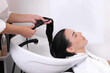 Professional hairdresser applying conditioner on woman's hair in beauty salon, closeup