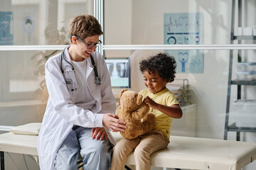 Pediatrist playing with toy with her little patient during medical exam at office