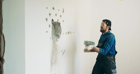 Wall Mural - A smiling guy demolishes a wall in a house using a construction hammer on a long stick. Fun demolition of an apartment during renovation, getting rid of an unnecessary wall gaining space.