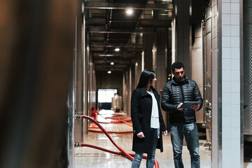 Caucasian couple during the winery visit, walking through the production industry cellar using a tablet to know the process of the winemaking