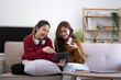 © wichayada - Two asian young woman happy smiling and using computer laptop on couch in living room at home