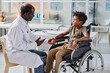 © AnnaStills - African doctor in white coat talking to little boy with disability during his visit at clinic