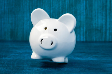 Wall Mural - White ceramic piggy-bank falling on the blue wooden background