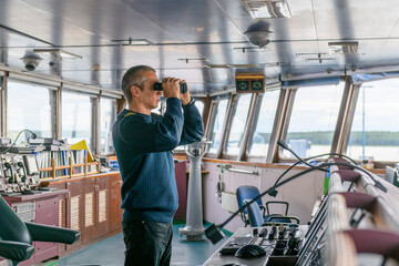 Wall Mural - Deck officer with binoculars on navigational bridge. Seaman on board of vessel. Commercial shipping. Cargo ship.