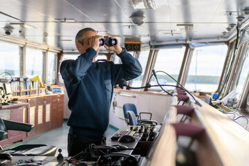 Wall Mural - Deck officer with binoculars on navigational bridge. Seaman on board of vessel. Commercial shipping. Cargo ship.