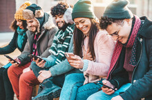 Millennial People Using Smart Mobile Phone Device Sitting Outside - Happy Teenagers Wearing Winter Clothes Hanging Out Together - Technology Lifestyle Concept