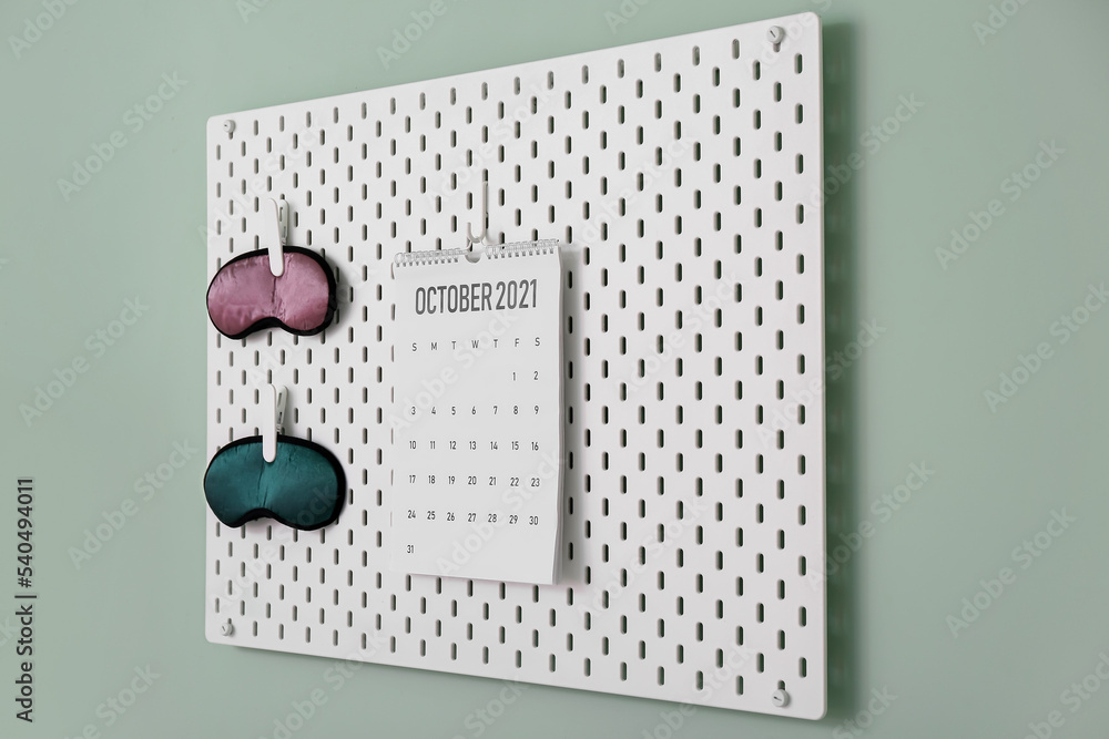 Pegboard with sleeping masks and calendar on color wall in room