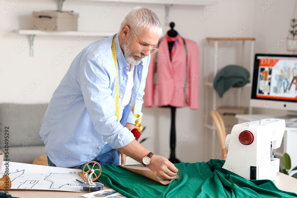 Mature fashion designer working with pattern and fabric at table in studio