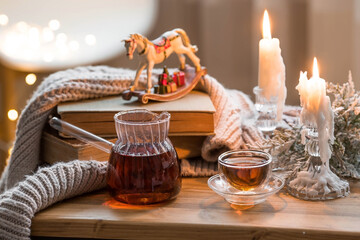 Wall Mural - Still-life. Old books, hot tea in a glass turk, a blanket and burning candles on a wooden table in a cozy living room. The concept of a tea ceremony. Home relaxation.