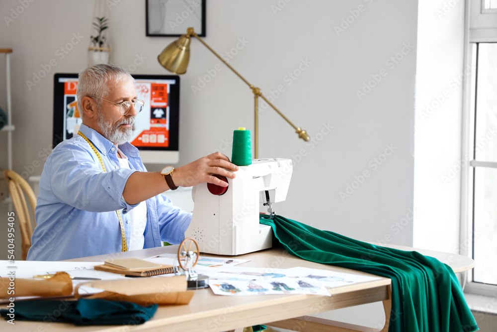 Mature fashion designer sewing cloth at table in studio