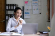 © wichayada - Beautiful young Asian businesswoman smiling holding a coffee mug and laptop working at the office.