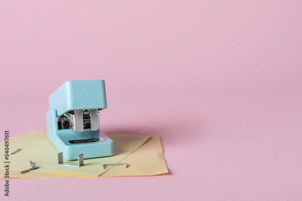 Stapler with sticky notes and staples on pink background