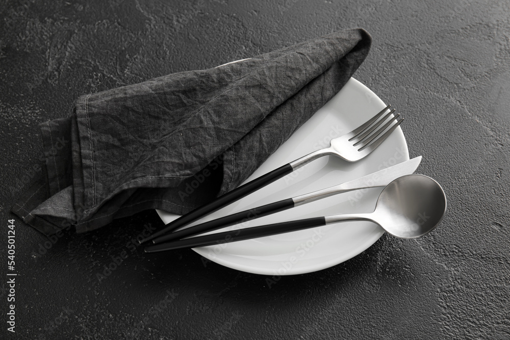 Table setting with cutlery and napkin in plate on dark background