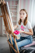 © Анна Молько - a girl in a white T-shirt paints with paints on a canvas on an easel. drawing at home.