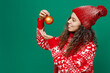 © ViDi Studio - Side view merry young woman wear red warm cozy knitted sweater hat posing hold Christmas tree decorations balls isolated on plain dark green background Happy New Year 2023 celebration holiday concept.