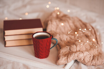 Wall Mural - Cup of tea with knit cloth sweater with Christmas lights and books in bed