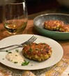 Vertical closeup shot of a plate with homemade crab cake and sauce near a glass of wine