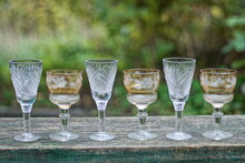 A Row Of White And Brown Glass Crystal Goblets On A Gray Wooden Table Outdoors On A Green Background