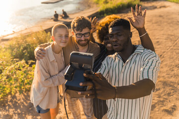 Wall Mural - Four beautiful multiracial people of different genders taking a selfie with analog instant camera during shiny sunset at the river. Creation of memories. High quality photo