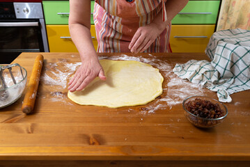 Women's hands are preparing dough for baking on the kitchen table in the home kitchen.