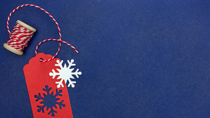 Wall Mural - red gift tag with snowflakes and red and white thread on spool. dark blue background.