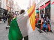 © mark_gusev - Man holding National flag of Ireland in focus. Grafton street of Dublin city out of focus in the background. Support or protest concept. Sun flare. Male with Irish flag.