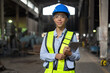 © amorn - Happy woman engineer worker working with digital tablet at the industry factory area. Female technician wear safety helmet, glasses and uniform checking and working in the factory