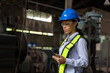 © amorn - Portrait of woman engineer worker working with digital tablet at the industry factory area. Female technician wear safety helmet, glasses and uniform checking and working in the factory
