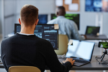 Wall Mural - Back view of male programmer or data specialist using computer in office with charts on screen, copy space