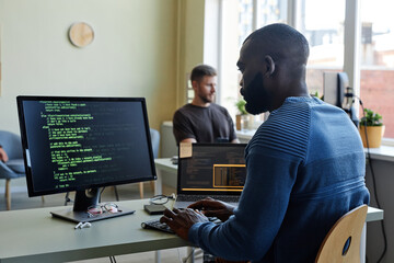 Wall Mural - Side view portrait of black software engineer writing code at workplace in office with multiple devices