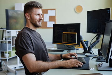 Wall Mural - Side view portrait of smiling Caucasian man as computer programmer writing code at office workplace