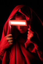 Portrait Of Young Man In Luminous Glasses Covering His Face With Mantle Against Black Background