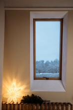 The Bedroom Is Decorated With A Christmas Tree And A Star, Has Beige Walls And A Wooden Window In The Wall. The Windows Overlook The Snowy Landscape.
