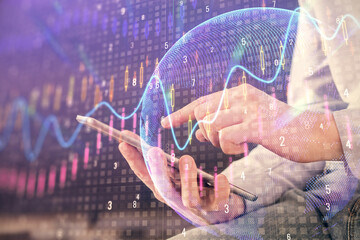 Double exposure of man's hands holding and using a digital device and forex graph drawing. Financial market concept.