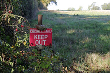A Red Sign By A Field In The Countryside Reads Private Land, Keep Out.
